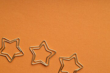 Star shaped paper clips on orange background, flat lay. Space for text