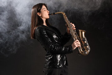 Beautiful young woman playing saxophone with smoke on dark background