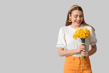 Happy young woman with bouquet of daffodil flowers on grey background