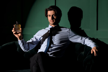 Young man holding bottle of perfume on dark green background
