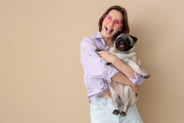 Young woman with cute pug dog on beige background