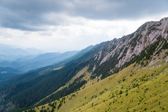 A Stunning Mountain Landscape With Rolling Hills, Dense Forests, And Dramatic Clouds Looming Overhead