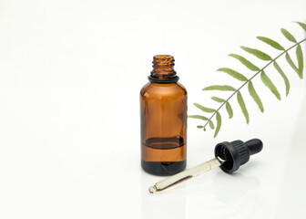 Amber glass dropper bottle and pipette with essential oil or serum for skincare with green leaf on white background