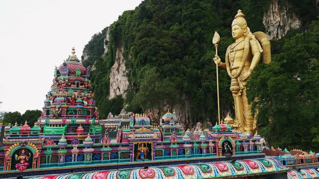 Golden murugan statue standing prominently at batu caves entrance, landmark hindu shrine near kuala lumpur, malaysia
