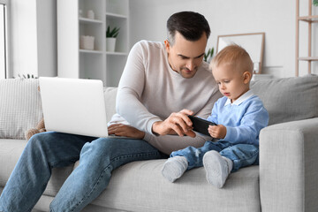 Father working while his little child playing with mobile phone at home