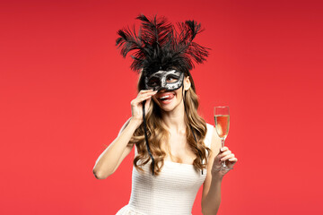 Playful woman lifting venetian mask and holding champagne glass during carnival party