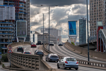 A dynamic city road filled with vehicles flows under a grey sky, surrounded by imposing skyscrapers that reflect the vibrant energy of urban life and movement in London