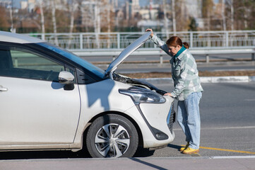 Caucasian woman looks puzzled under the hood of a car. 