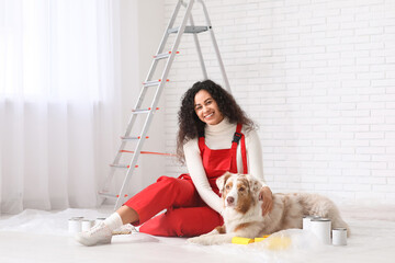 Happy female African-American painter in uniform with equipment and cute Australian Shepherd dog sitting during repair at home