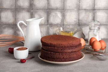 Delicious chocolate sponge cake cut into layers with ingredients and kitchen utensils on grey grunge background