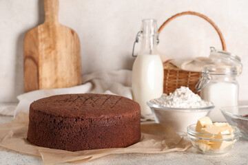 Delicious chocolate sponge cake with flour, butter and bottle of milk on light grunge background