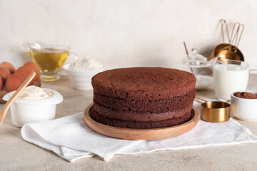 Delicious chocolate sponge cake cut into layers with ingredients and kitchen utensils on light background