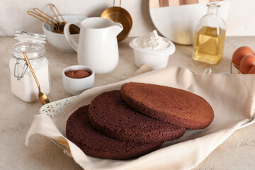 Delicious chocolate sponge cake cut into layers with kitchen utensils and ingredients on light grunge background