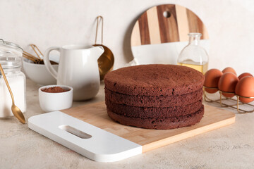 Delicious chocolate sponge cake cut into layers with kitchen utensils and ingredients on light grunge background