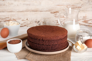 Delicious chocolate sponge cake cut into layers with ingredients on light wooden background
