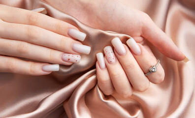 Woman showing stylish white nails with red glitter and diamond ring on silk fabric