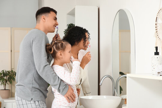 Little girl and her parents brushing teeth near mirror in bathroom
