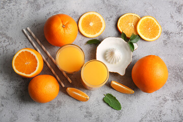 Glasses of fresh orange juice with fruits and juicer on grey background