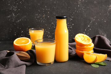 Bottle and glasses of fresh orange juice with mint on black background