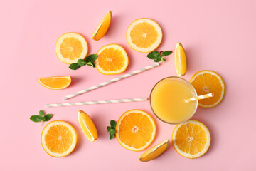Glass of fresh orange juice with mint and cut fruit on pink background