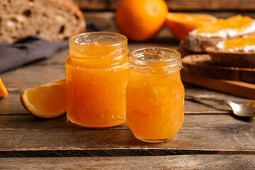 Jars of sweet orange jam on wooden background