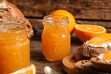 Jars of sweet orange jam and slices of bread on wooden background