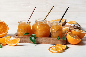 Jars of sweet orange jam and fruits on white wooden background