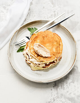 A stack of fluffy pancakes sits on a rustic plate, garnished with a creamy spread. Natural light fills the bright kitchen, creating a warm, inviting atmosphere perfect for breakfast