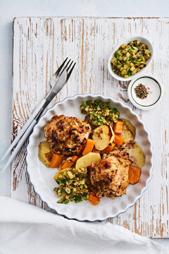 Roasted chicken thighs are plated with golden potatoes, carrots, and a fresh salsa made from diced pickles. The meal is set on a rustic wooden surface, creating an inviting atmosphere