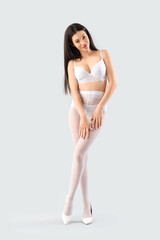 Fototapeta premium Attractive young woman in underwear and white tights on light background