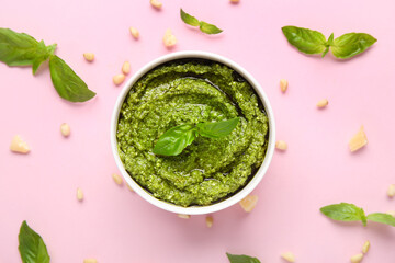 Bowl of delicious pesto sauce with basil leaves, pine nuts and cheese on pink background