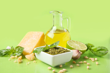 Bowl with delicious pesto sauce, jug of oil and ingredients on green background
