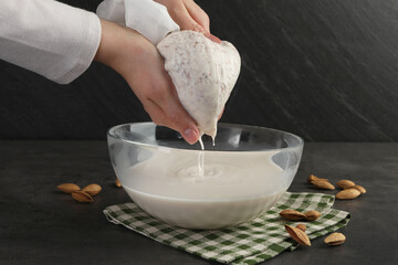Woman making almond milk and nuts at black table, closeup