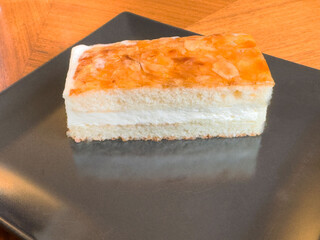 Almond topped cream cake slice on black plate