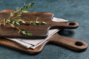 Empty cutting boards with napkin and eucalyptus branch on dark blue grunge table, closeup