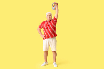 Sporty senior man exercising with kettlebell on yellow background