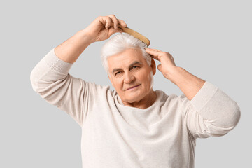 Senior man combing hair on grey background. Hair loss concept