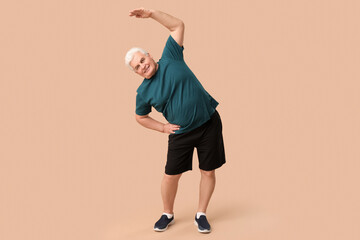 Sporty senior man exercising on beige background