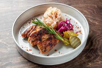 Grilled meat served on a stylish plate, accompanied by pickled vegetables, sauerkraut, and fresh herbs. A flavorful dish perfect for food lovers and culinary presentations.