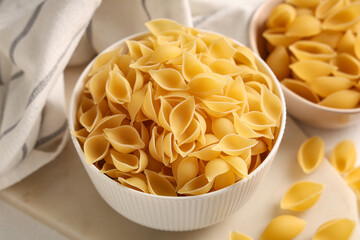 Bowl and tray with raw pasta shells on white background, closeup