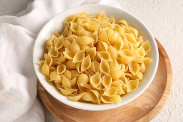 Bowl with raw pasta shells on white background
