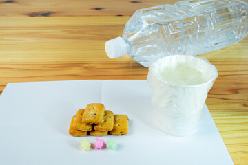 ビニール袋でカバーされた水が入った紙コップと避難所配給品の一食分の乾パン