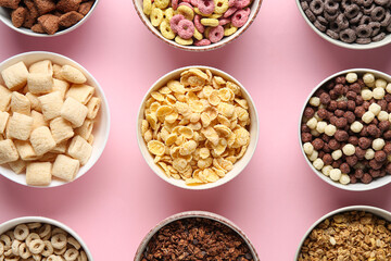 Bowls with different cornflakes on pink background