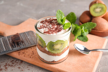 Glass with delicious kiwi cheesecake on grey grunge background