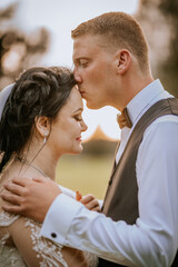  A groom tenderly kisses the bride’s forehead during a golden hour outdoor wedding. Love, intimacy, and warmth captured in a serene moment.