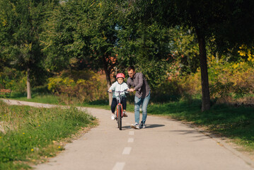Fototapeta premium Father teaching daughter riding bicycle in park during summer day