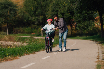 Naklejka premium Father teaching daughter riding bicycle in park during sunny day