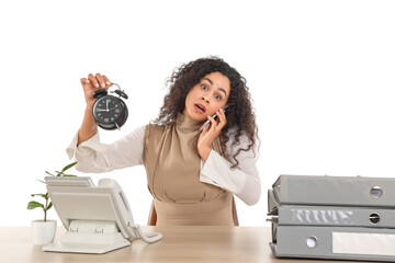 Stressed African-American businesswoman with alarm clock talking by mobile phone at table on white...