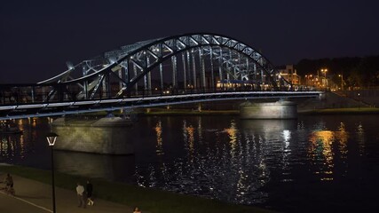 Bridge illuminated at night with reflections in river and people enjoying the riverside stroll - Powered by Adobe
