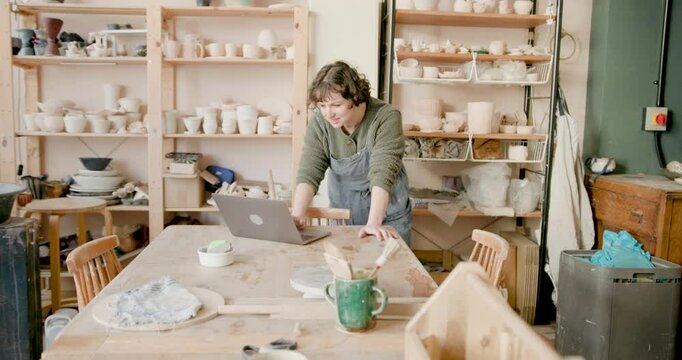 Artist in Apron using Laptop in Pottery studio setting